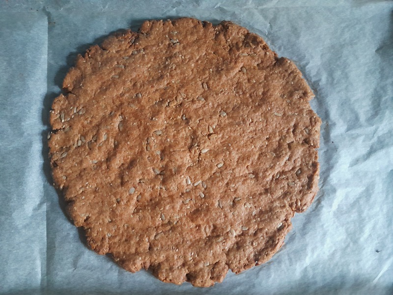 Roughtly oval shaped baked cracker on baking paper on a baking tin